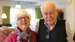 En årsrik kvinna med glasögon och vitt kortklippt hår samt en äldre herre i väst och skjorta som står bredvid varandra och skrattar på träffpunkt Norrehed i Löddeköpinge