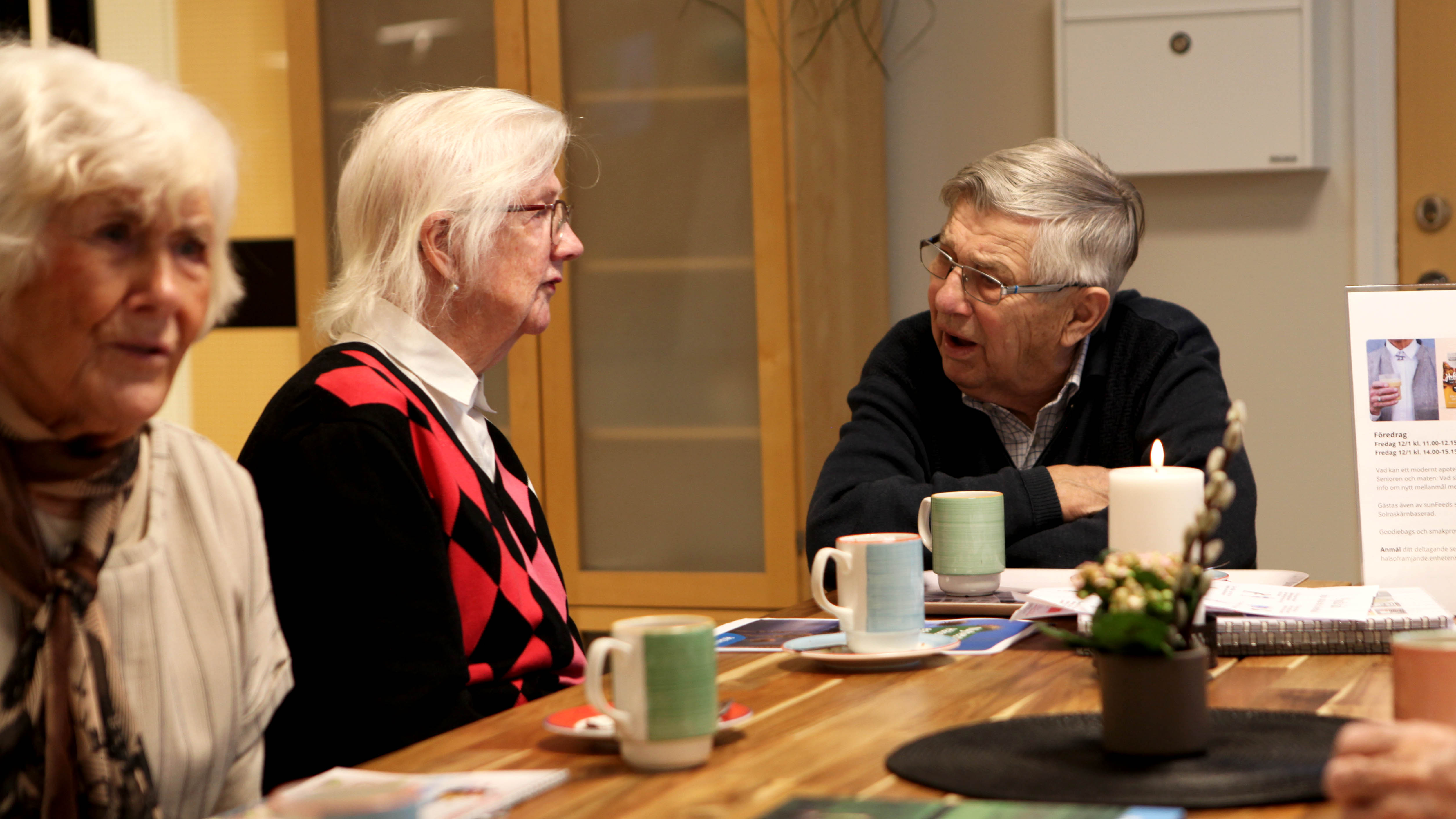 Äldre man och kvinna sitter vid ett träbord och diskuterar. 