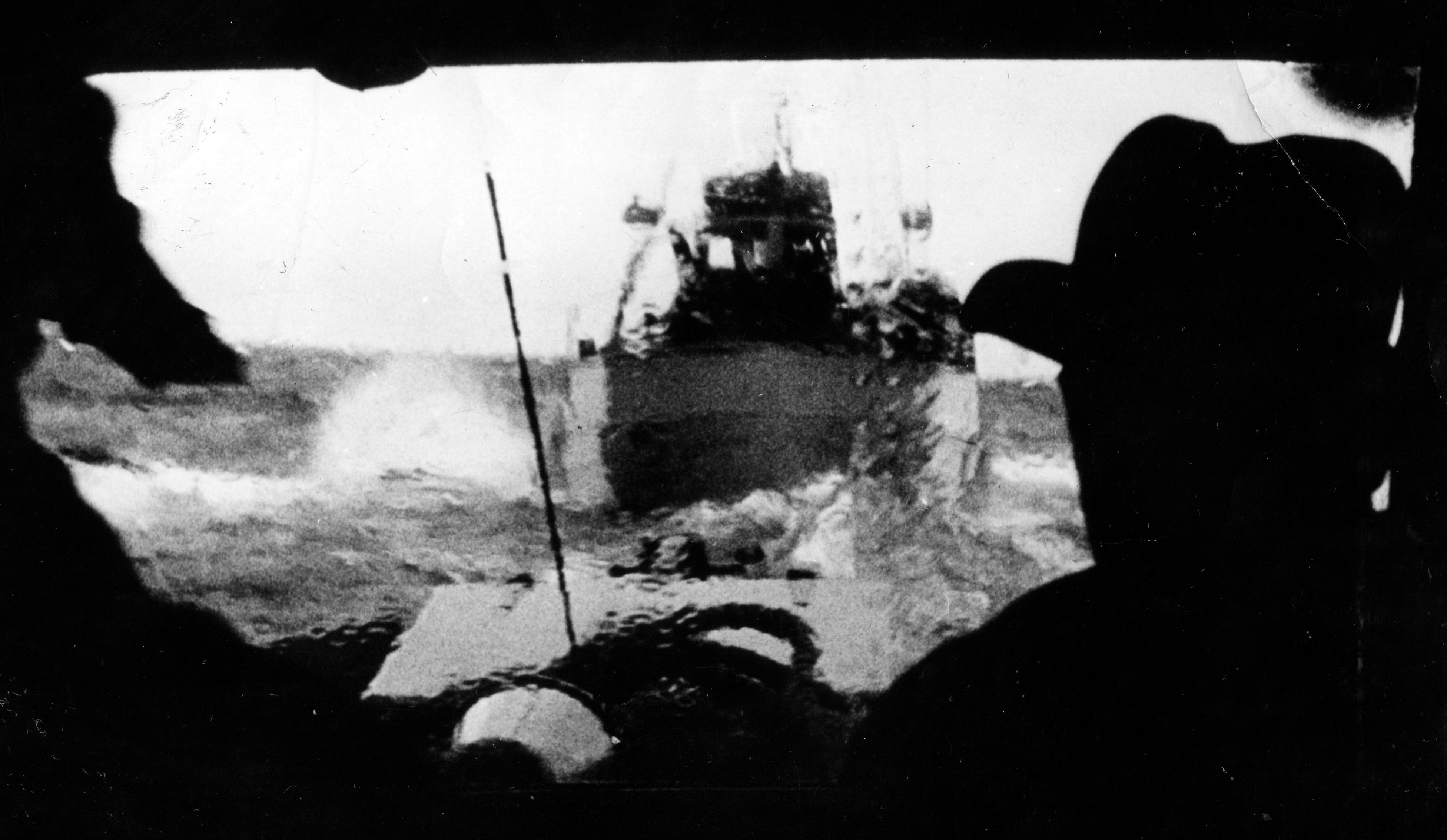 Svartvitt foto med 2 fiskebåtar till sjöss. I förgrunden en man i svart rock med utsträckta armar.