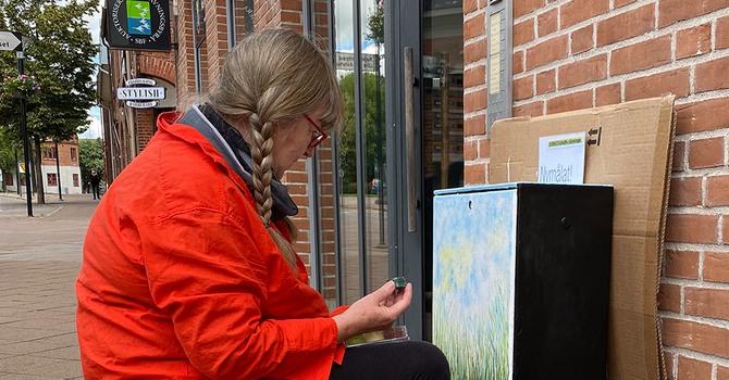 En konstnär i orange målarrock målar ett elskåp i Kävlinge cemtrum.
