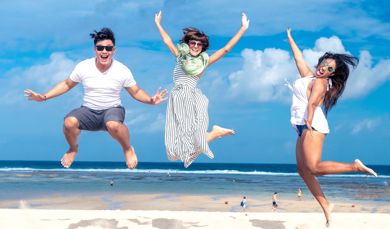 Tre ungdomar fotade i luften då de hoppar på en strand.