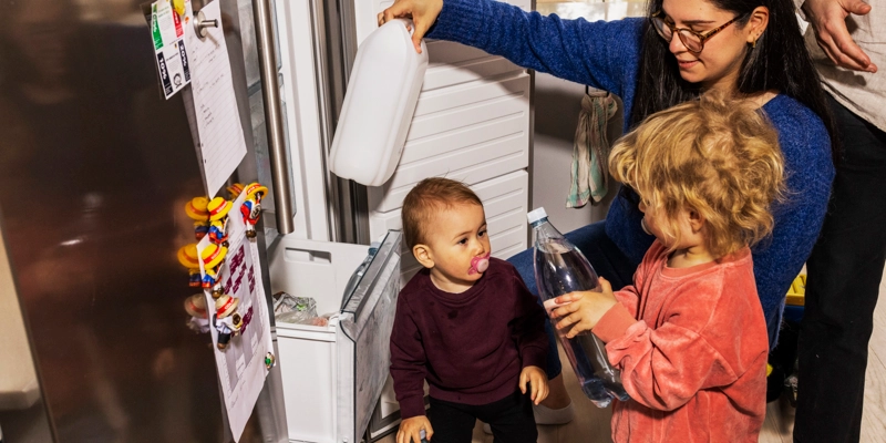 En mamma med två barn packar in vattendunkar i frysen.