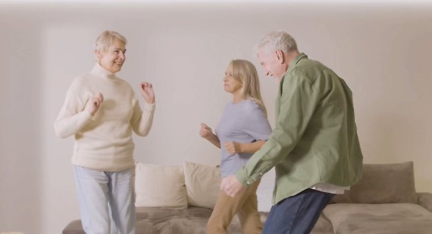 Tre äldre personer dansar loss i ett vardagsrum